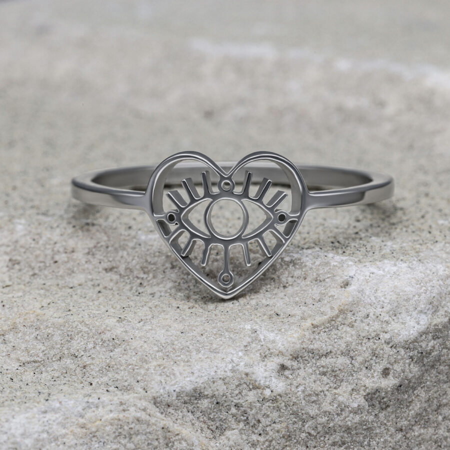 Silberner herzförmiger Ring mit Auge-Motiv auf grauem Stein