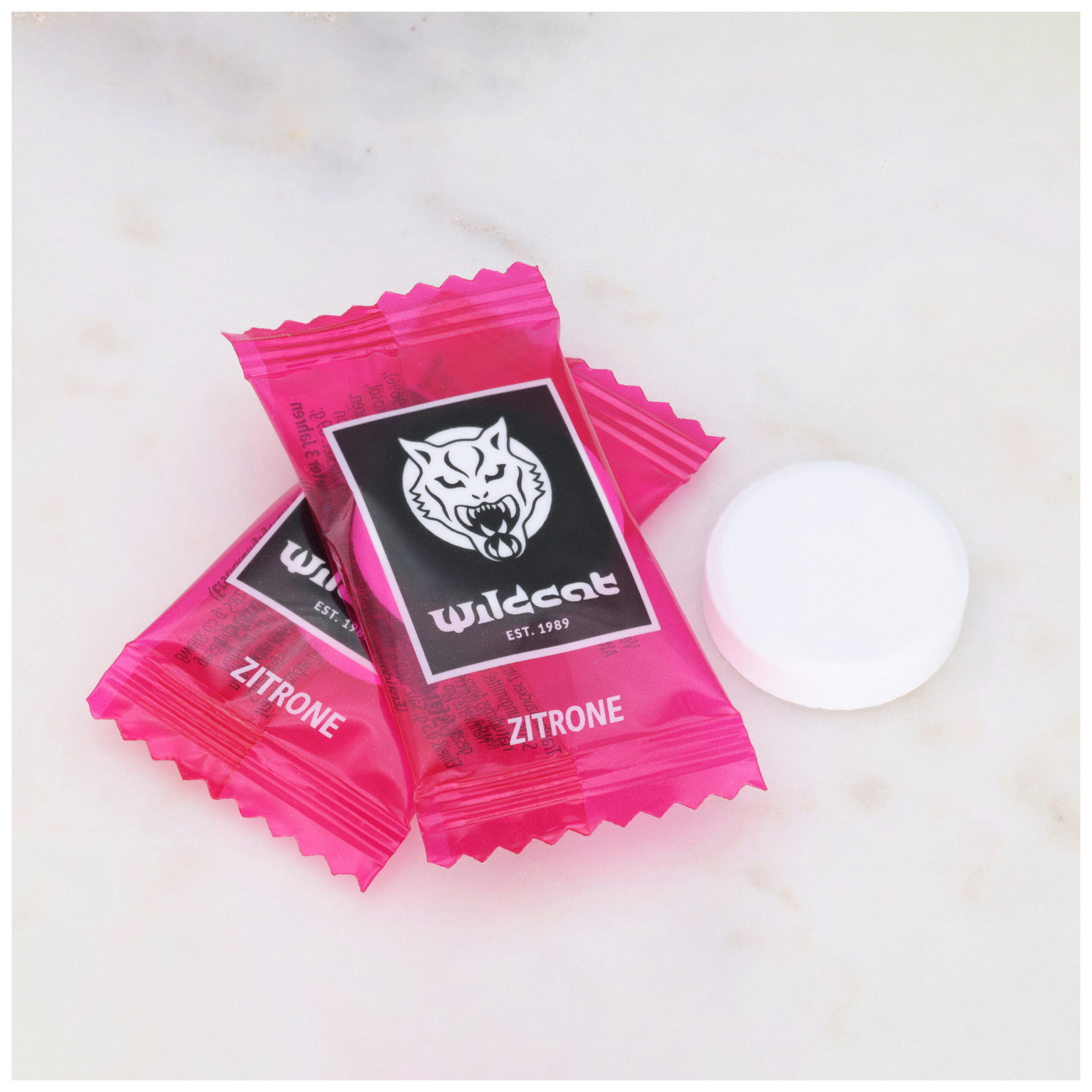 Wildcat Zitronen-Dextrosetabletten 1000 Stk. Zwei pinke Wildcat Zitronen-Dextrosetabletten auf Marmorhintergrund