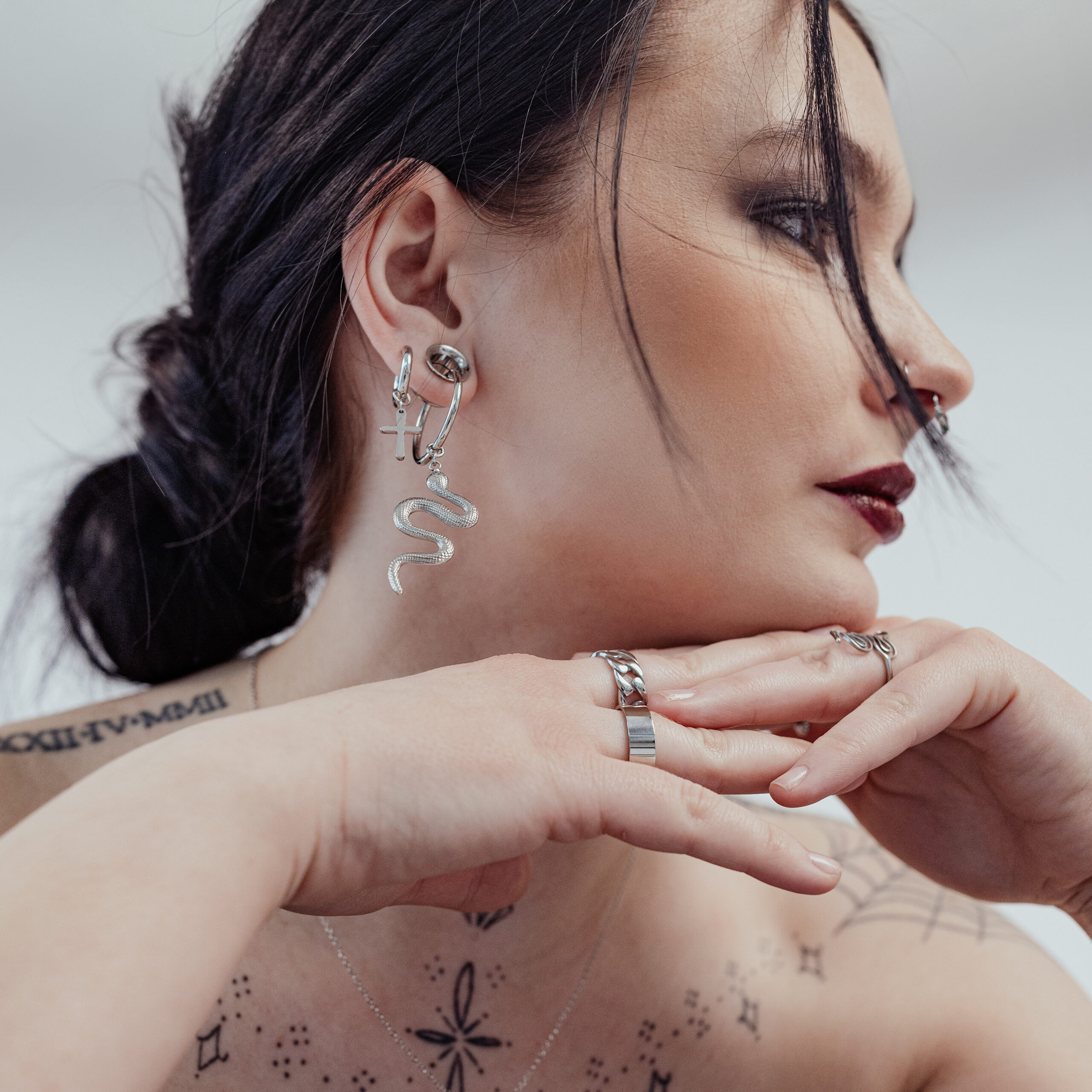 Silberne Little Cross Hoops am Ohr einer Frau Frau mit silbernen Little Cross Hoops und Schlangenohrring, weißer Hintergrund