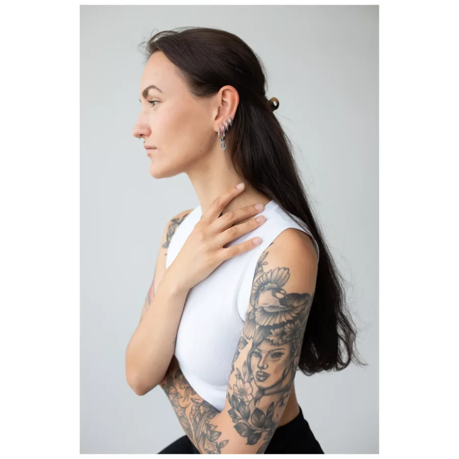 Frau mit langen Haaren und tätowierten Armen, trägt silberne Little Anchor Hoops Ohrringe