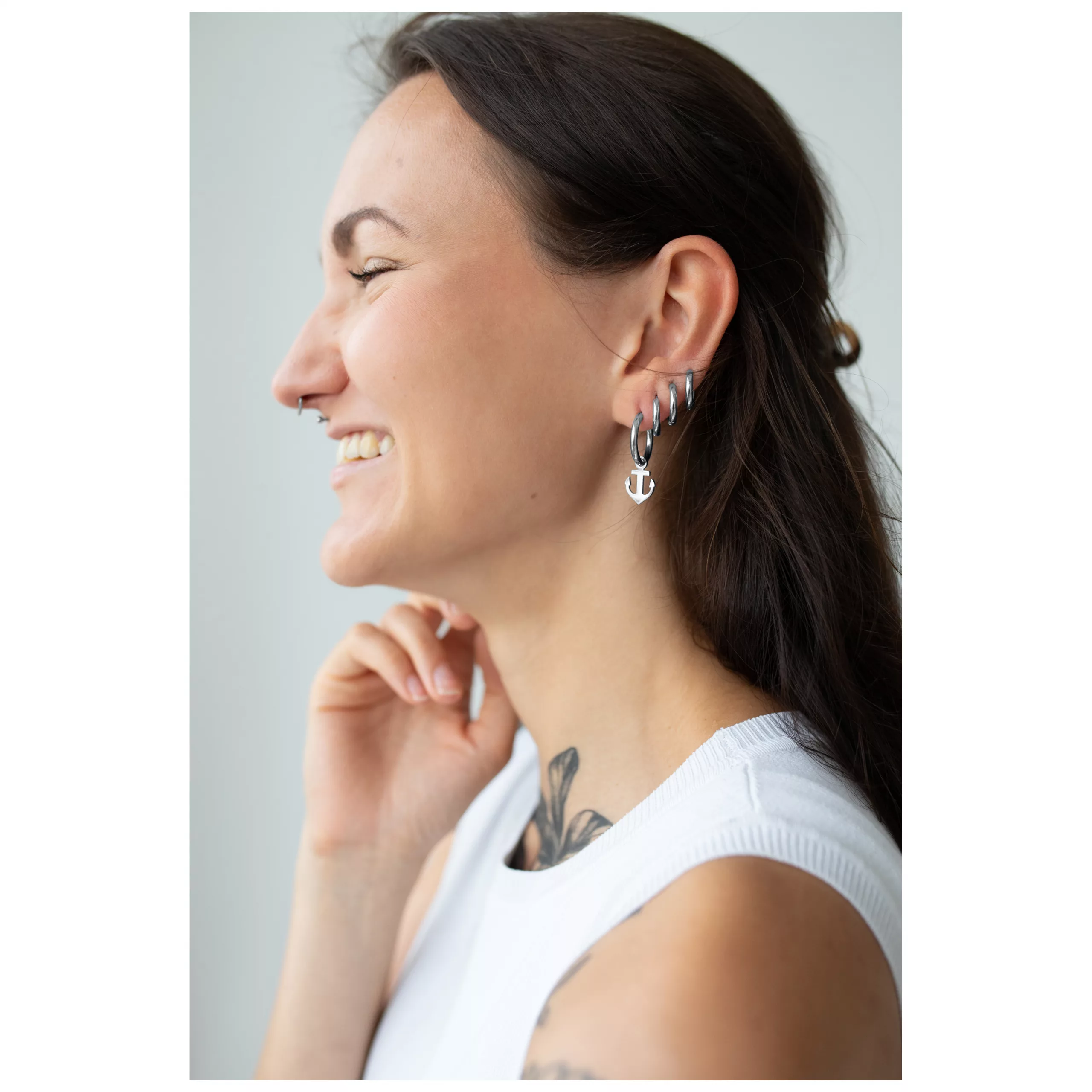 Damen mit Little Anchor Hoops Ohrringen Frau mit langen dunklen Haaren trägt silberne Anker-Ohrringe und lächelt