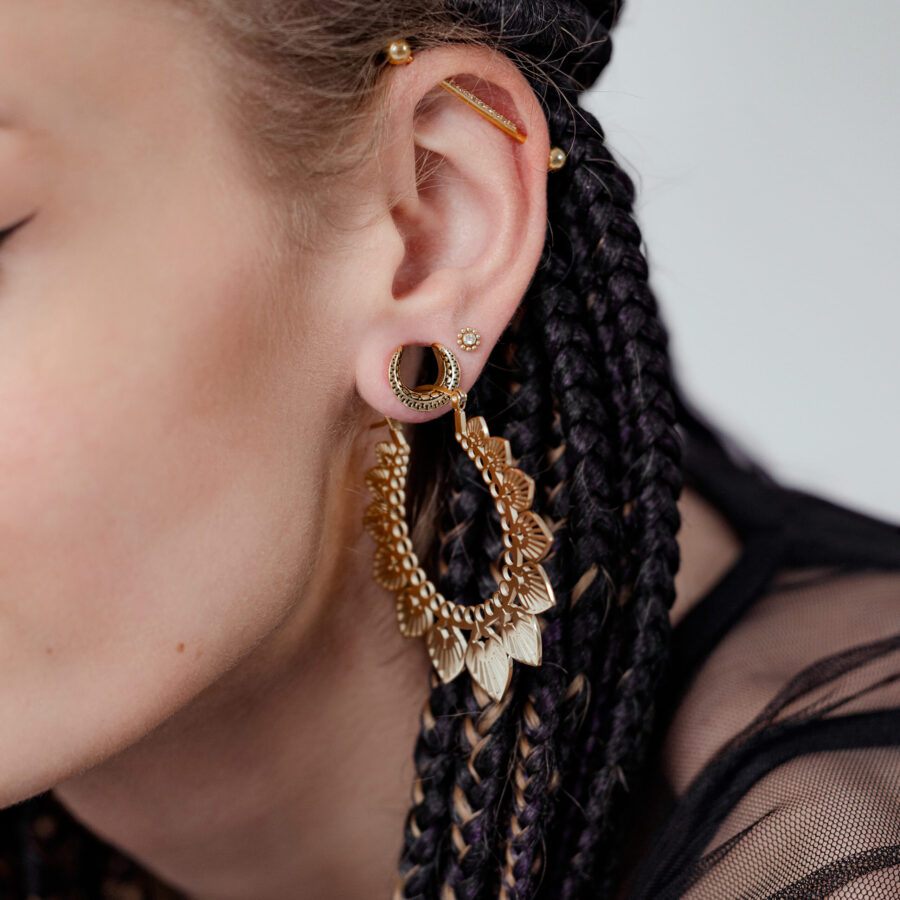 Nahaufnahme eines Ohres mit geflochtenem Haar, das einen goldenen Titan Kristall Blütenaufsatz für Innengewinde mit 2,5 mm Kugel zeigt