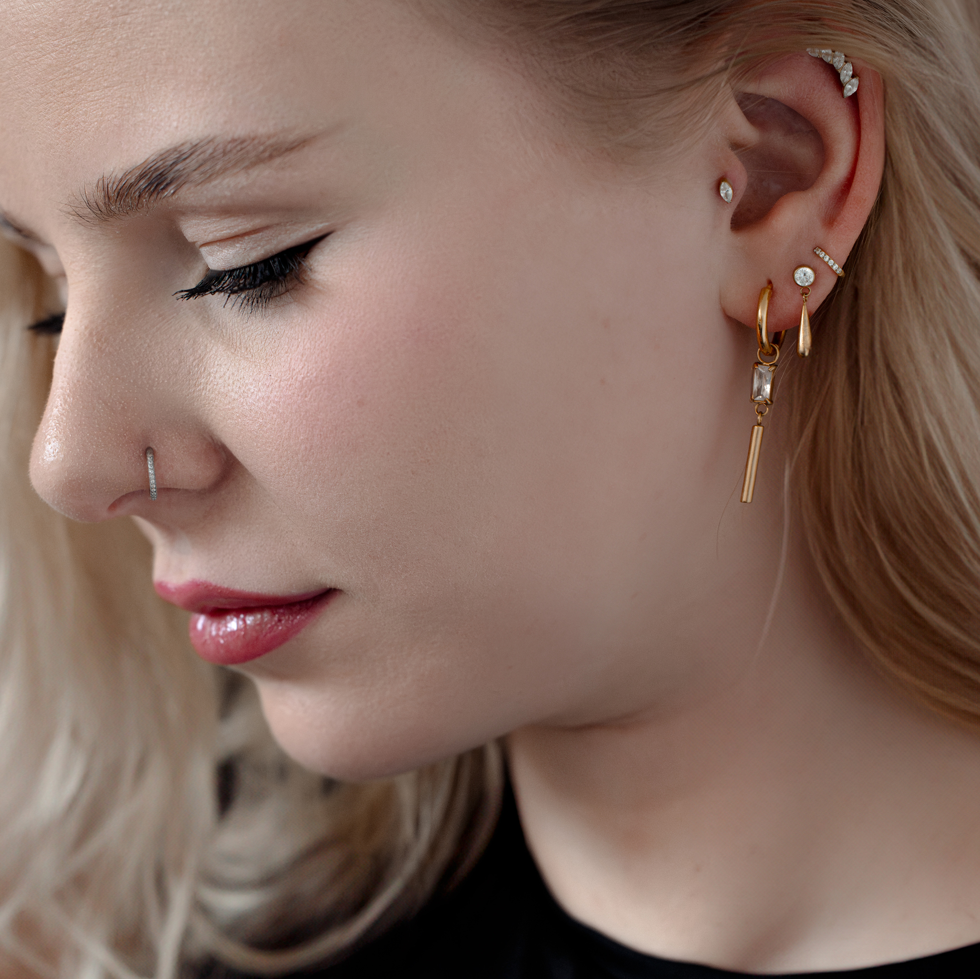 Eleganter Kristall-Piercingaufsatz im Ohr Frau mit mehreren Piercings, darunter ein goldener Kristall-Piercingaufsatz im Ohr.