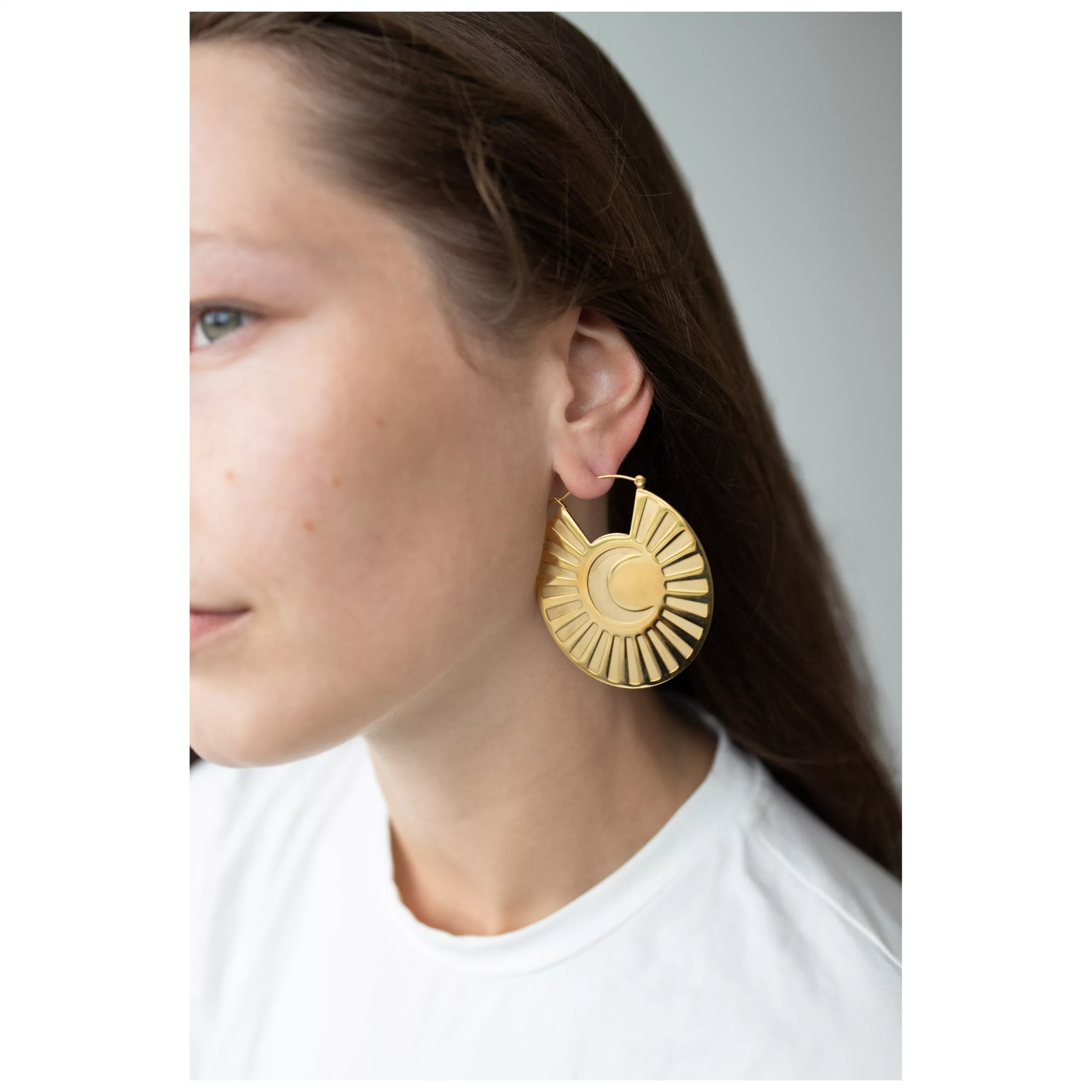 Goldene Moonshine Hoops Ohrringe am Ohr Frau mit langen Haaren trägt goldene Ohrringe in Sonnenform