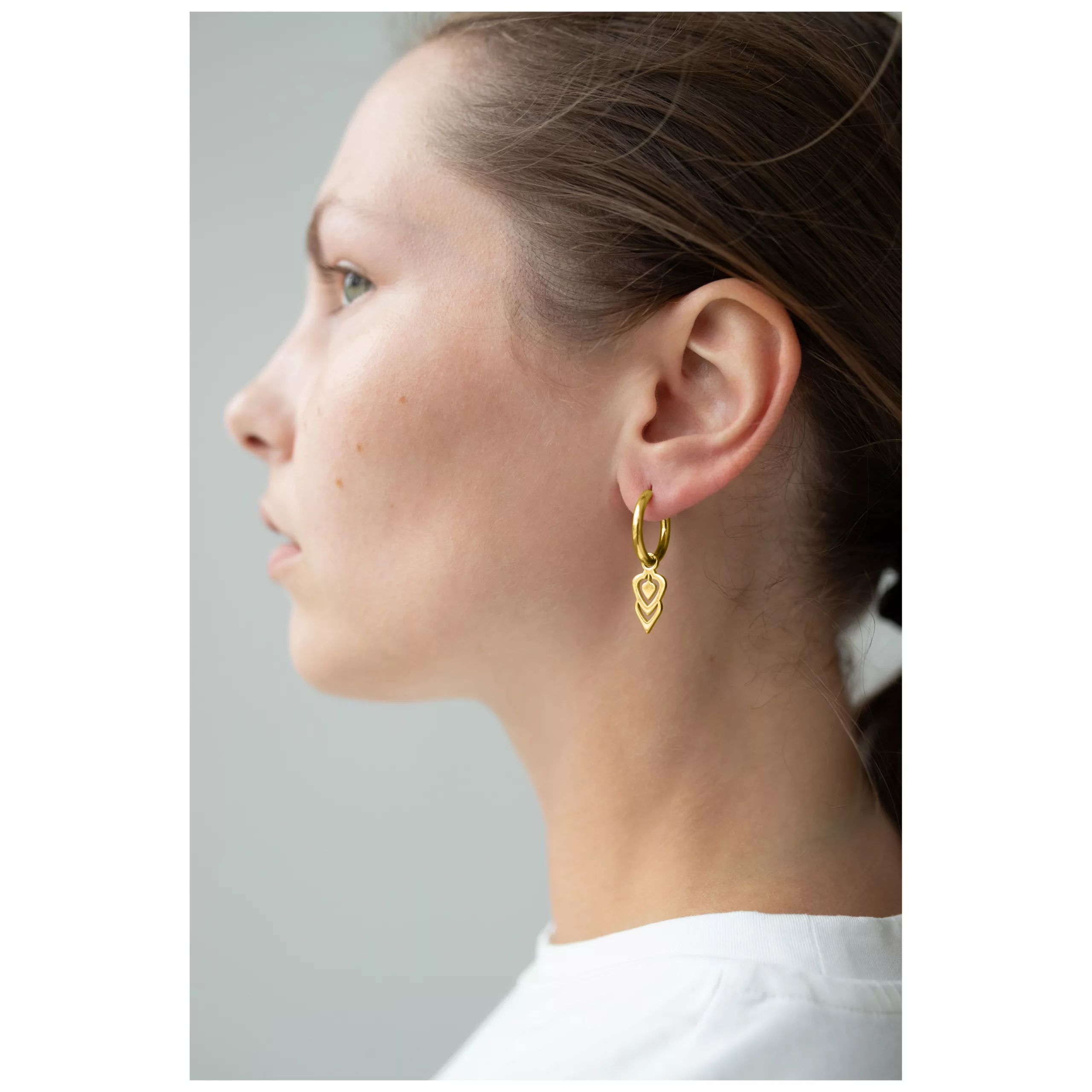 Goldene Little Balisuta Hoops im Profil Frau mit goldenen Little Balisuta Hoops Ohrringen vor neutralem Hintergrund