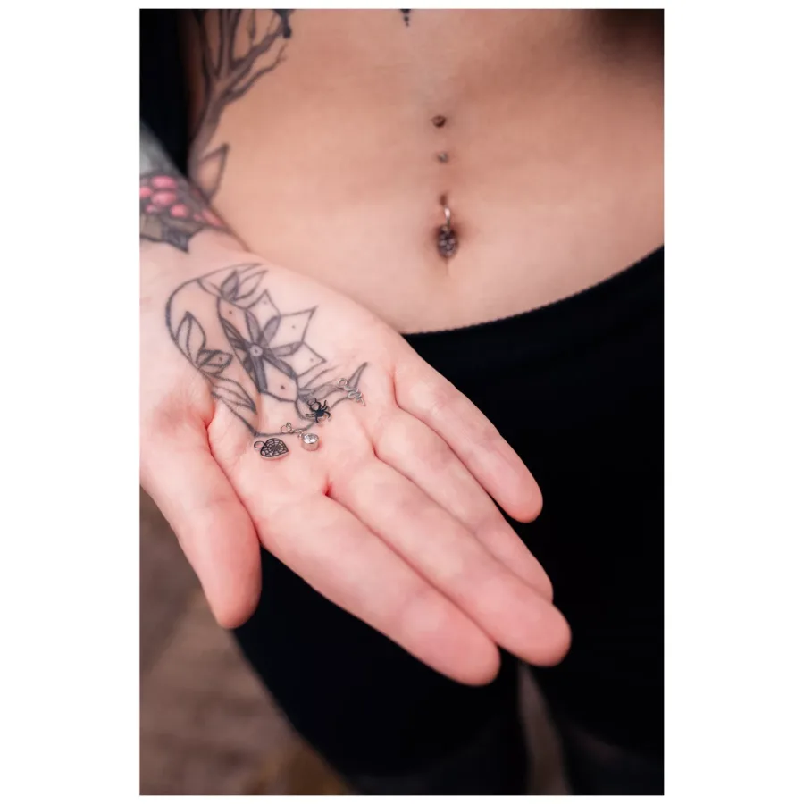 Hand mit schwarzen Bauchnabelringen, tätowierter Arm, Bauchnabelpiercing sichtbar