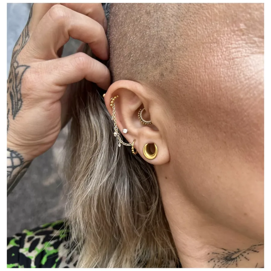 Goldener Piercingring mit kleinen Kristallkugeln an einem Ohr mit mehreren Piercings.