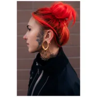 Frau mit roten Haaren trägt goldene Kaleidoscope Hoops vor einer Backsteinwand