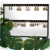 Schwarzes Ohrring-Display mit Pflanzen Schwarzes Ohrring-Display mit goldenen Ohrringen, umgeben von grünen Blättern