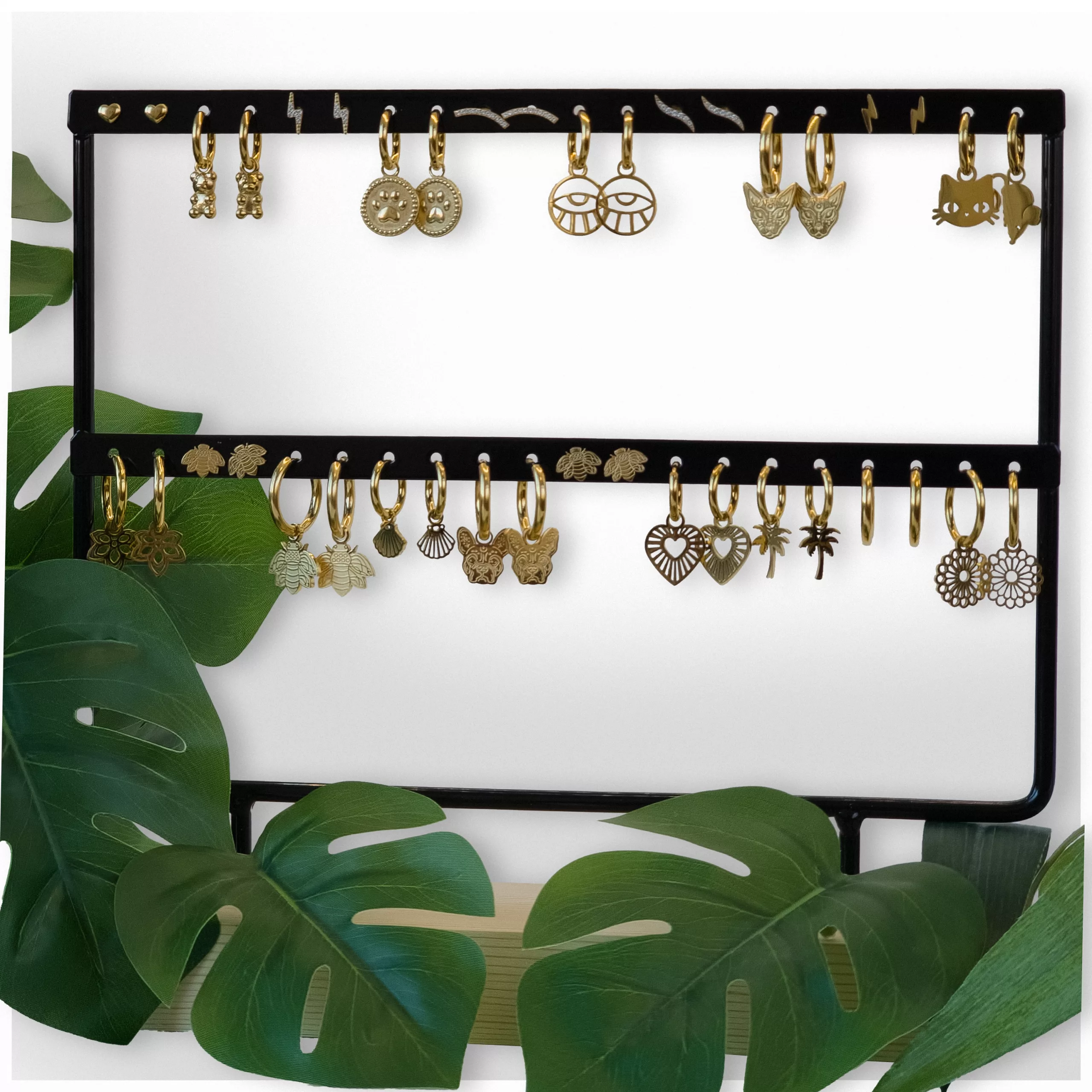 Schwarzes Ohrring-Display mit Pflanzen Schwarzes Ohrring-Display mit goldenen Ohrringen, umgeben von grünen Blättern