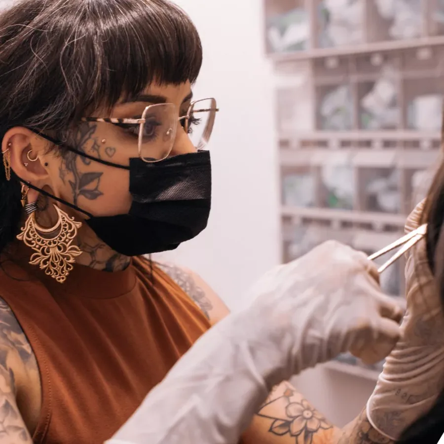 Frau mit Tattoos, goldenen Ohrringen und schwarzer Maske arbeitet konzentriert