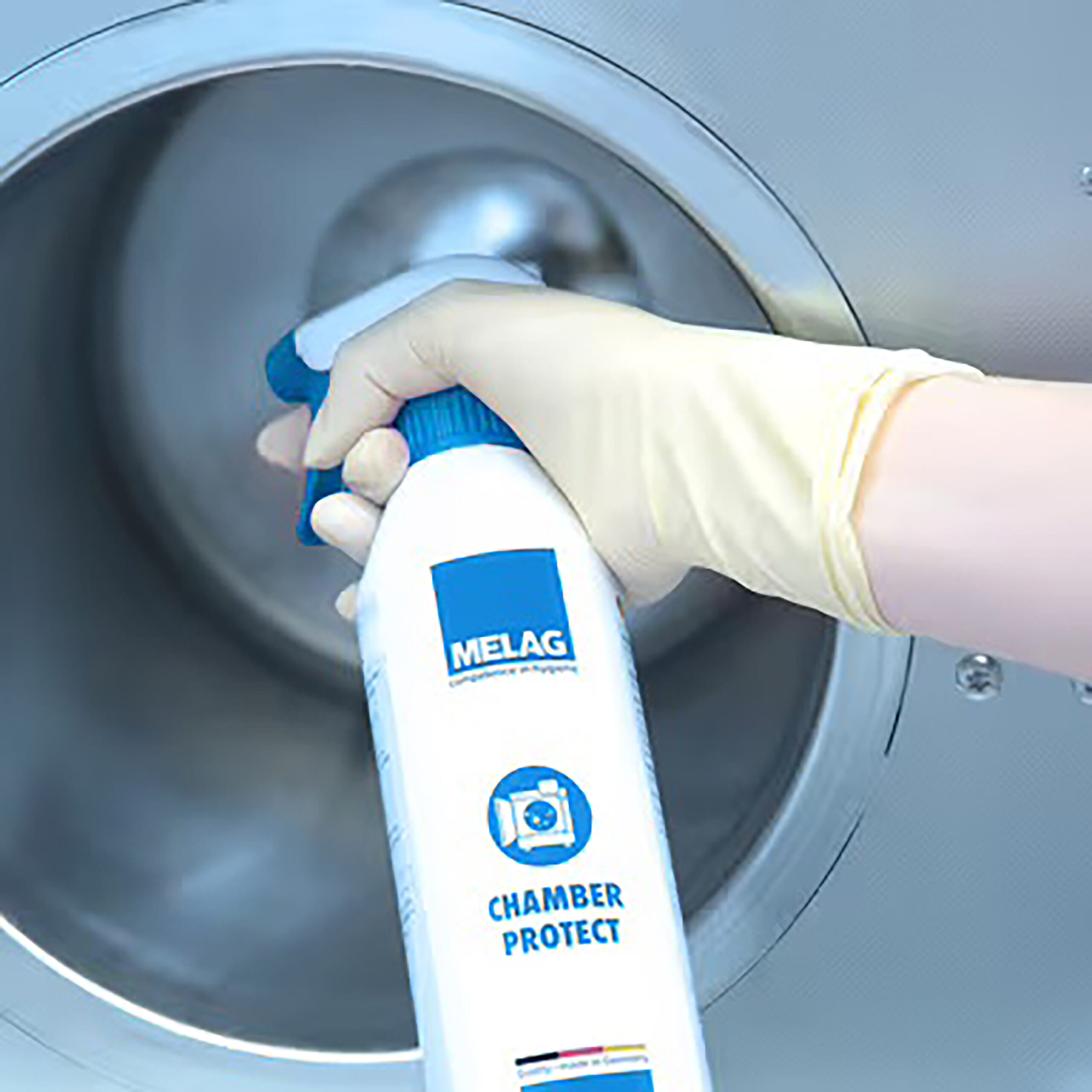 Chamber Protect Kesselreinigungsset mit Sprühflasche Hand mit gelbem Handschuh hält Sprühflasche Chamber Protect vor rundem Metallkessel