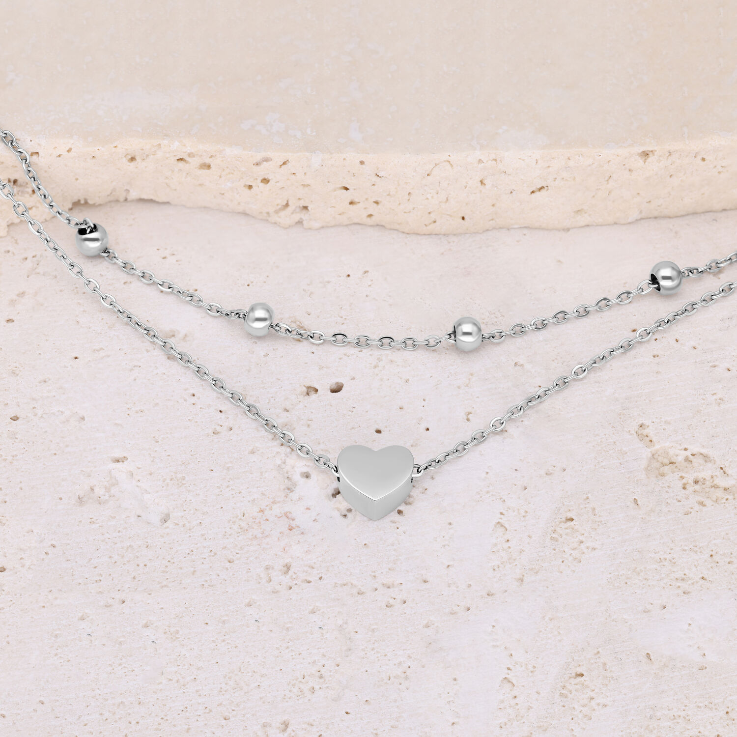 Doppelreihiges Herzarmband aus Edelstahl Silbernes doppelreihiges Armband mit Herz und Kugeln auf hellem Hintergrund
