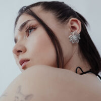 Elegante Blumen-Ohrstecker aus Edelstahl Frau mit eleganten Blumen-Ohrsteckern aus silbernem Edelstahl vor weißem Hintergrund