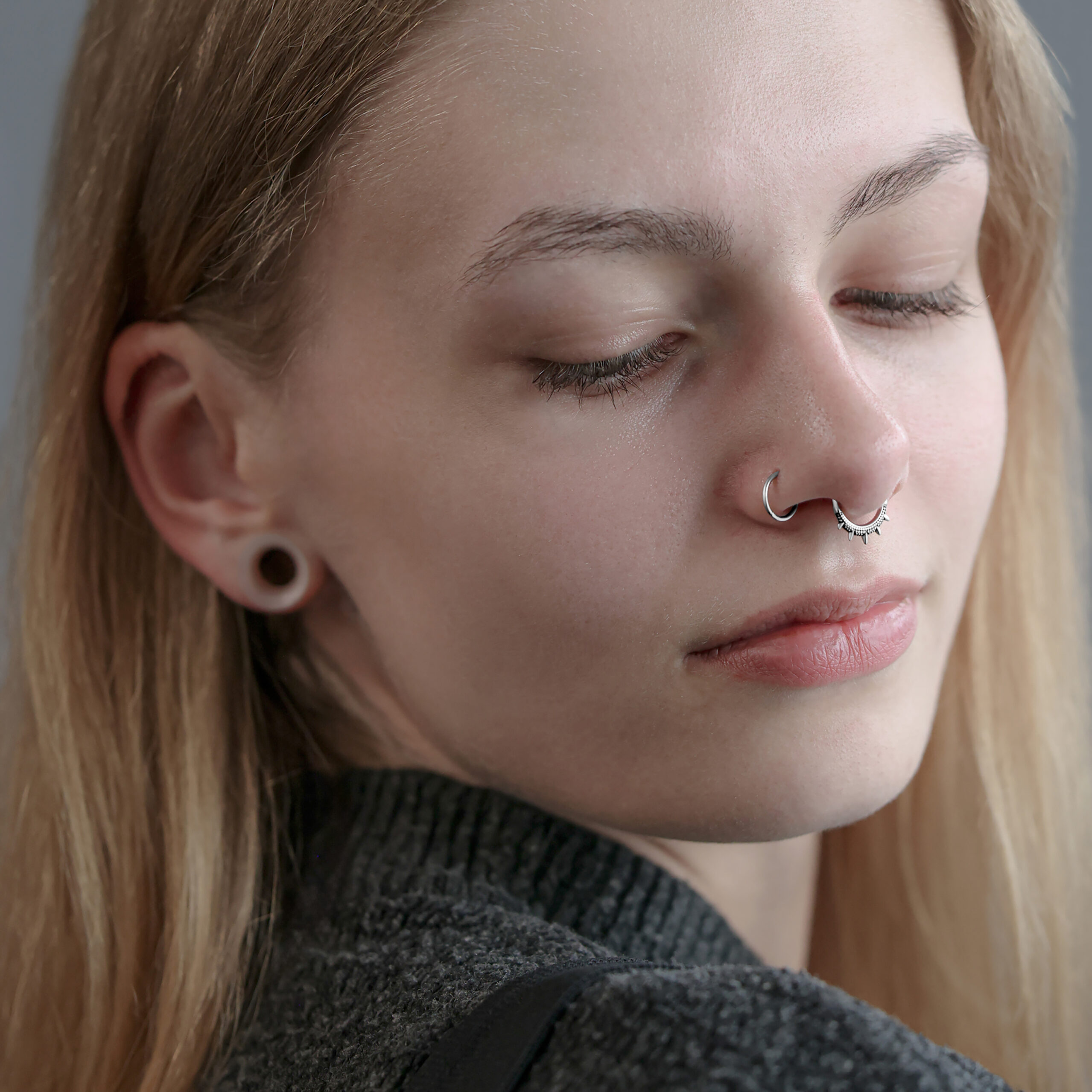 Oriental Spiked Clicker in Silber am Septum Frau mit silbernem Septum Clicker und gedehnten Ohrläppchen auf grauem Hintergrund