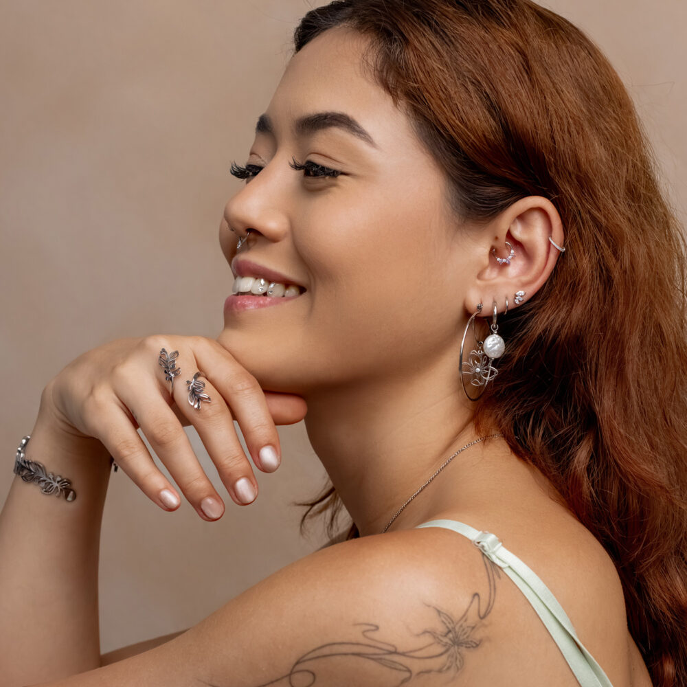 Frau mit roten Haaren und mehreren silbernen Ohrringen und Piercings, beige Hintergrund