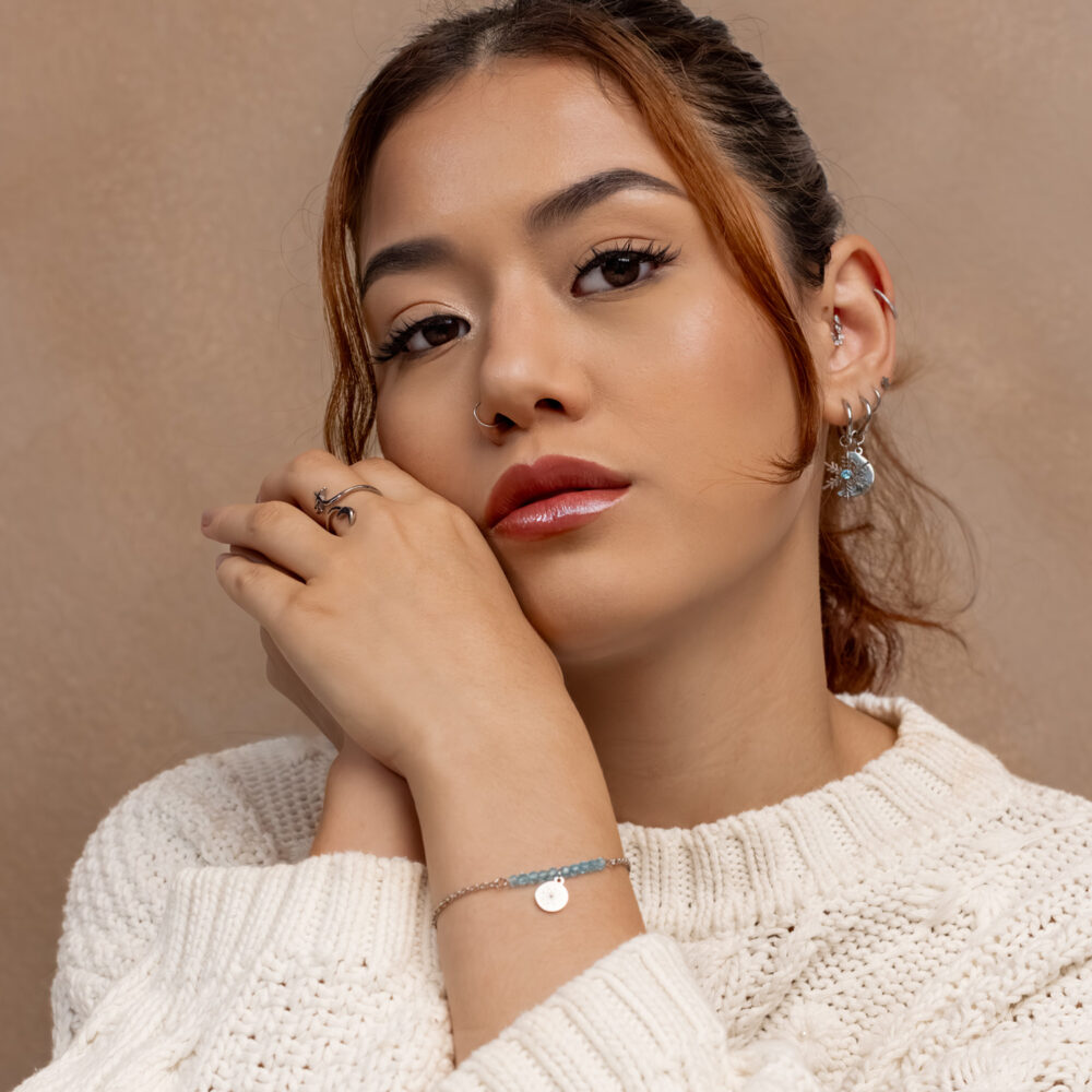 Frau in cremefarbenem Pullover mit Ohrringen, Armband und Ring in Blau und Silber