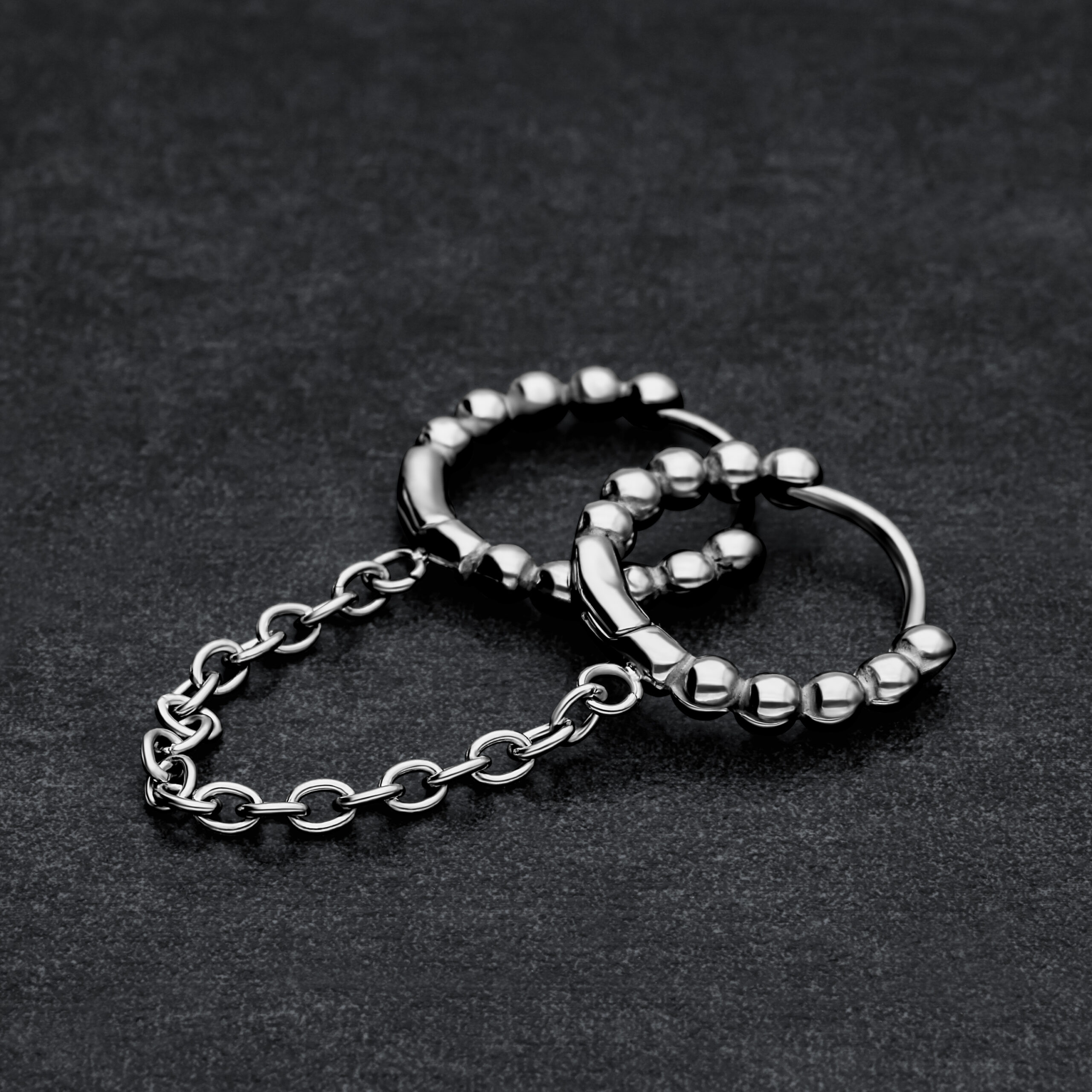 Zwei verbundene schwarze Huggie Piercingringe mit Kugeln auf dunklem Hintergrund