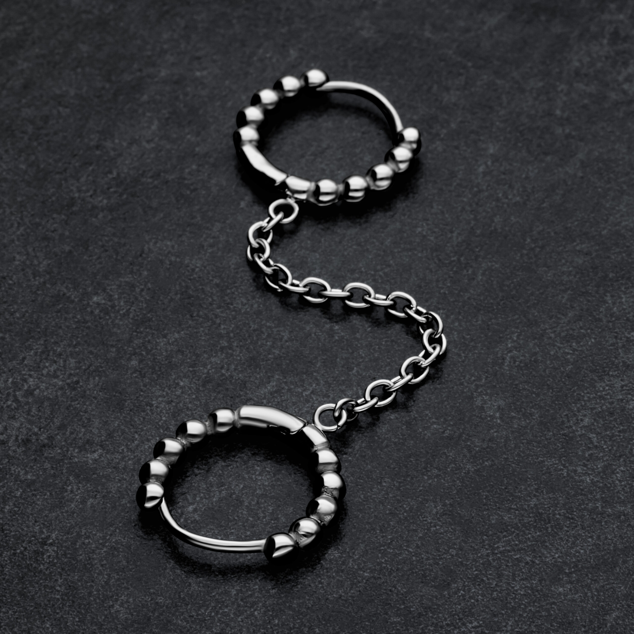 Silberne Double Huggie Ball Hoops mit Kettenverbindung auf dunklem Hintergrund