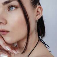 Eleganter Push Fit Blumenaufsatz mit Kristallen Frau mit Push Fit Blumenaufsatz im Ohr, silberne Kette und Ohrringe, weißer Hintergrund
