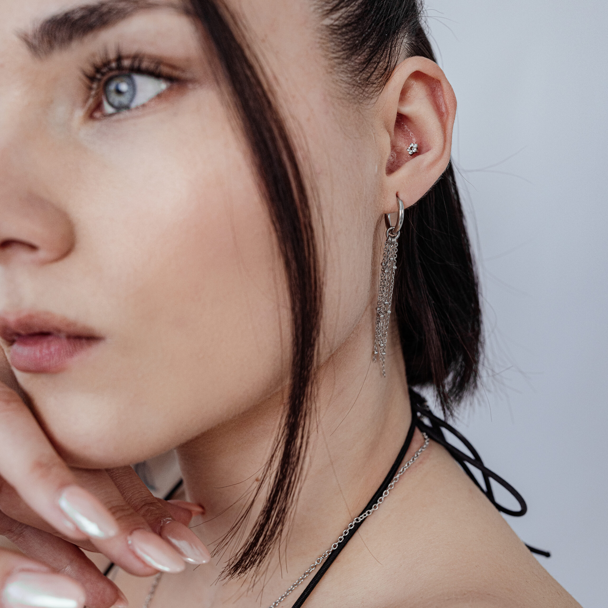 Eleganter Push Fit Blumenaufsatz mit Kristallen Frau mit Push Fit Blumenaufsatz im Ohr, silberne Kette und Ohrringe, weißer Hintergrund