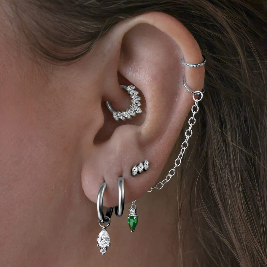 Mehrere Ohrringe im Ohr, darunter schwarze Little Tear Hoops mit grünem Kristall.