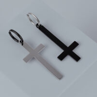 Zwei Kreuz-Ohrringe aus Chirurgenstahl in Gold und Schwarz auf grauem Hintergrund