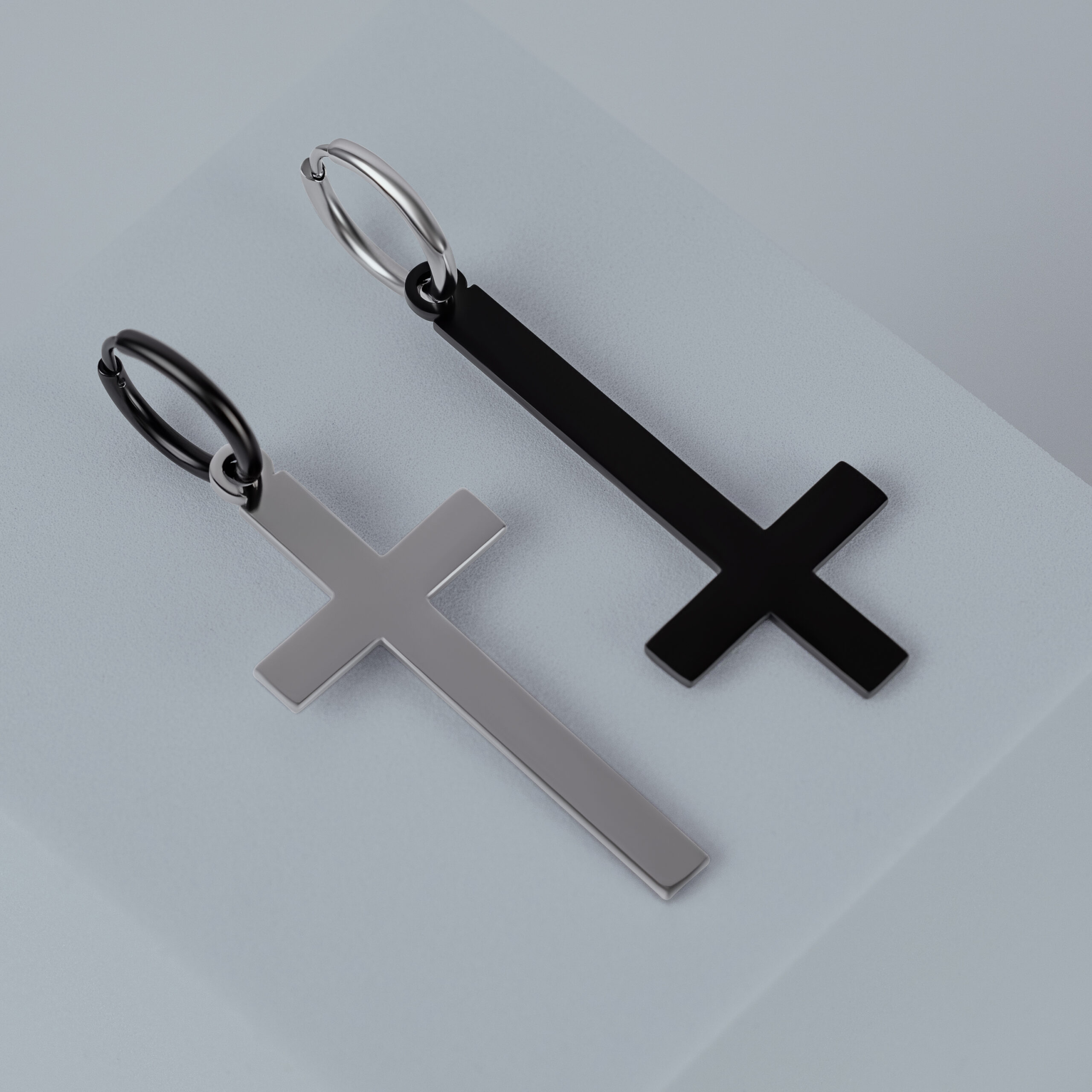 Zwei Kreuz-Ohrringe aus Chirurgenstahl in Gold und Schwarz auf grauem Hintergrund