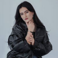 Unisex Kettenring in Silber und Gold Frau mit schwarzer Lederjacke trägt silbernen Kettenring und passendes Armband auf grauem Hintergrund