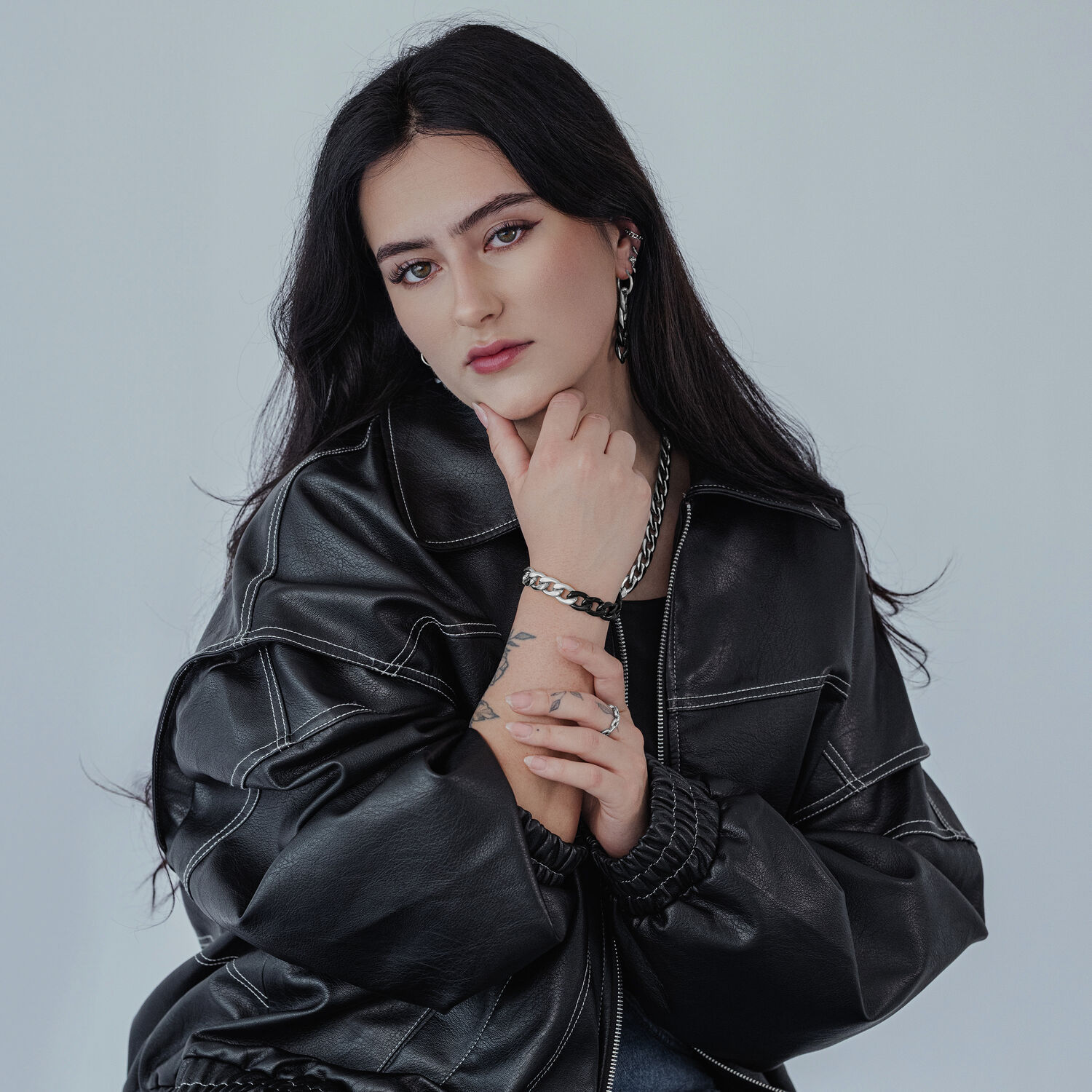 Unisex Kettenring in Silber und Gold Frau mit schwarzer Lederjacke trägt silbernen Kettenring und passendes Armband auf grauem Hintergrund