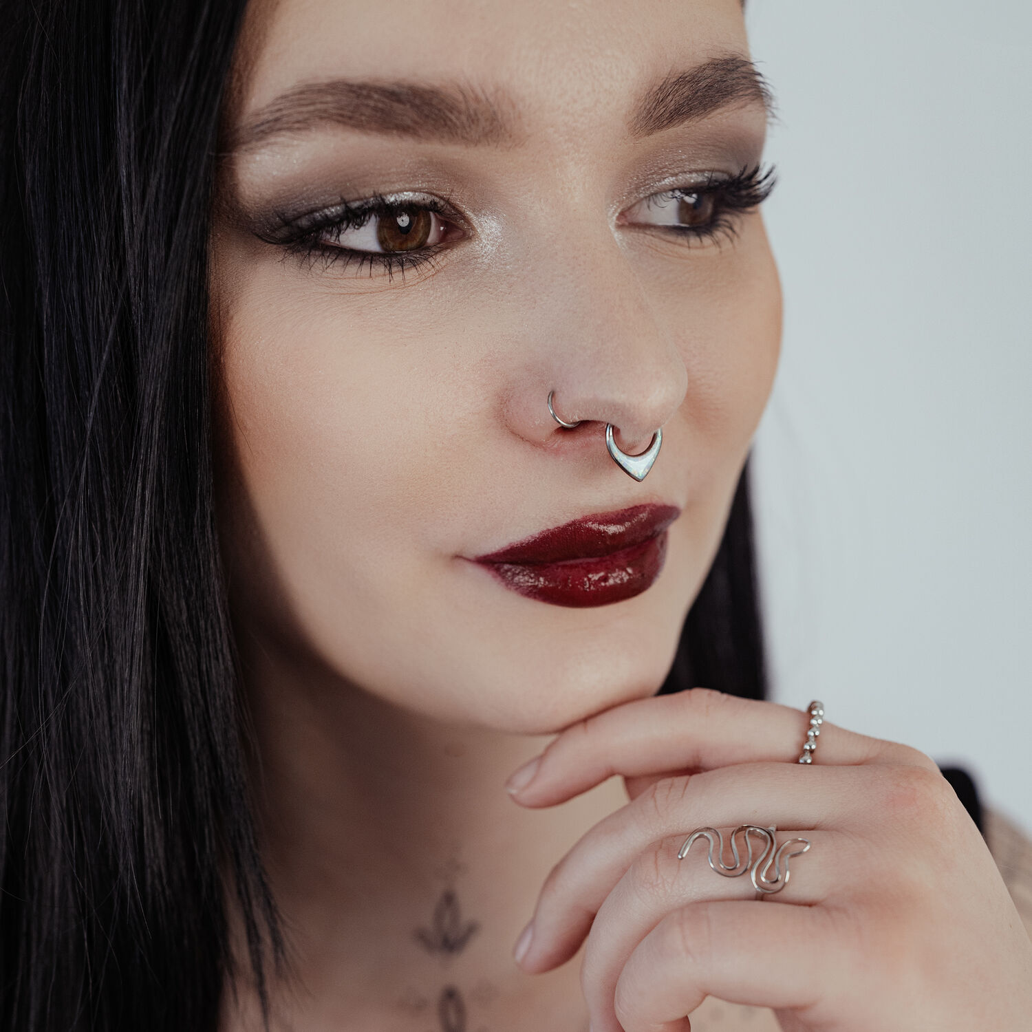Frau mit schwarzem Haar trägt silbernen Septum Clicker mit Opal auf hellem Hintergrund