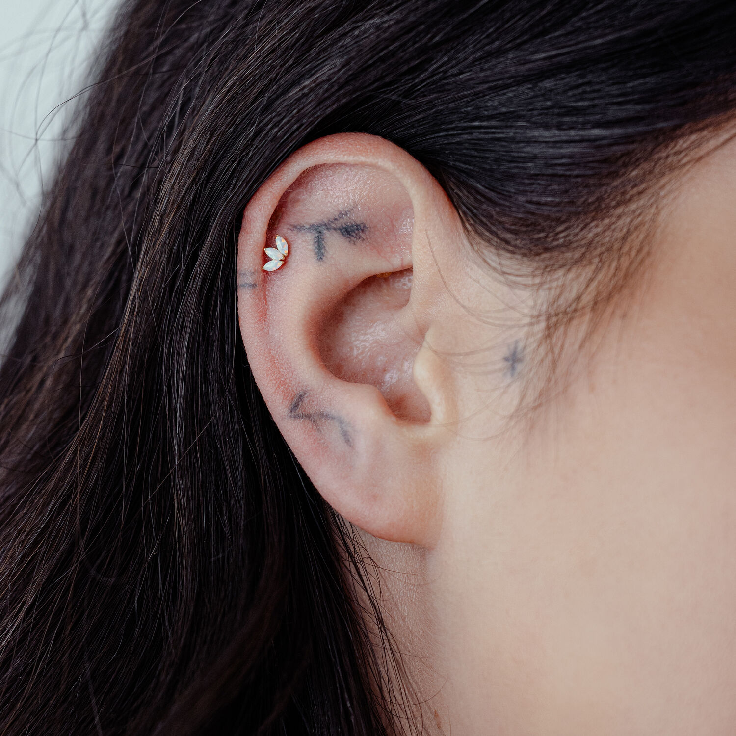 14K Gold Lotus Opal Ohrpiercing Nahaufnahme eines Ohrpiercings mit 14K Gold Lotus und synthetischem Opal an einem Ohr