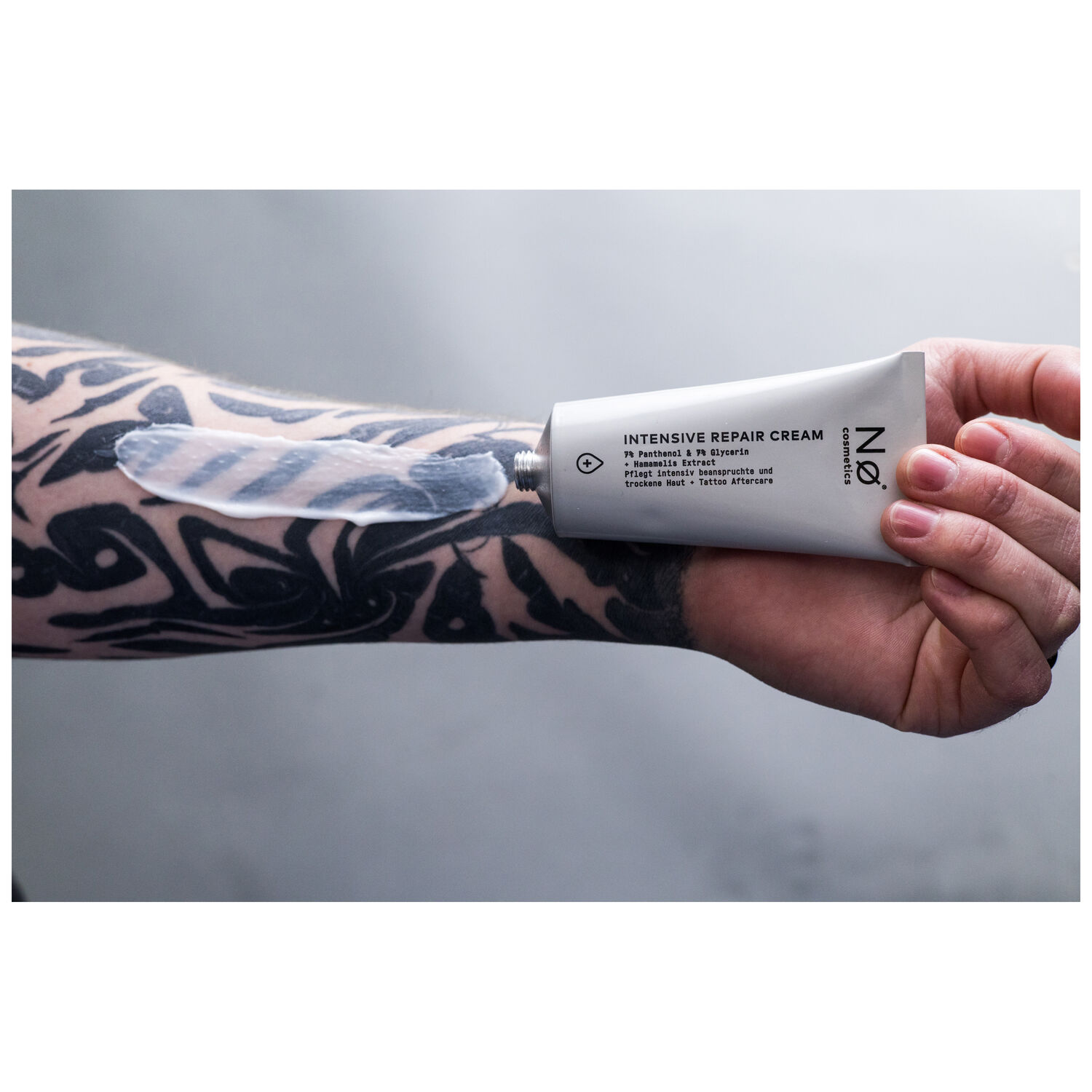 Grau-weiße Tube der Intensiv Repair Cream von No Cosmetics, gehalten von tätowierter Hand