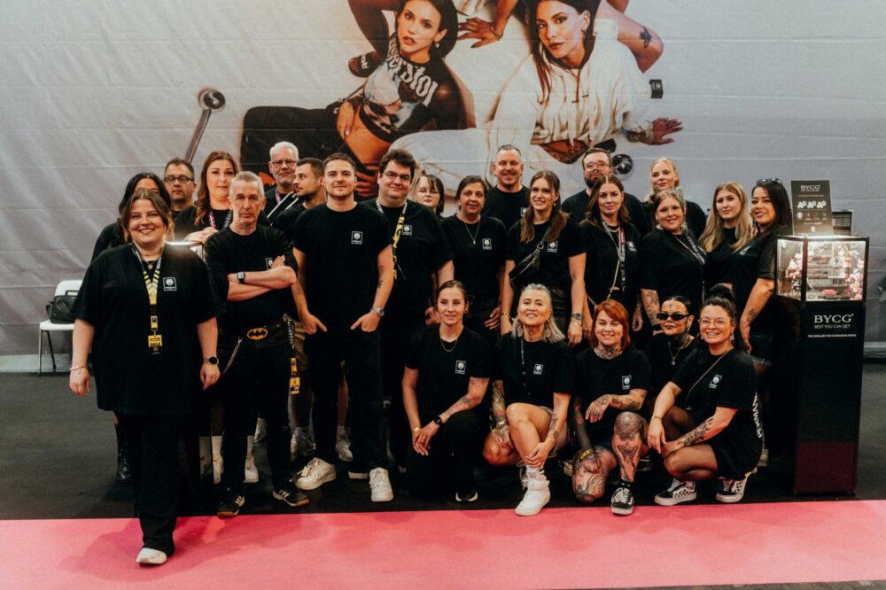 Gruppe von Personen in schwarzen T-Shirts vor einem großen Poster auf der Dortmund Tattoo Convention