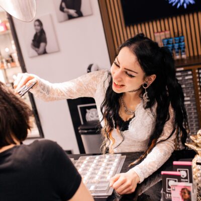 Piercerin mit langen dunklen Haaren in weißem Top berät Kunden im Studio