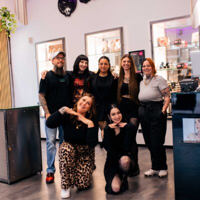 Gruppe von sieben Personen in einem Piercing- und Schmuckgeschäft. Lächelnd, vor Vitrine mit Produkten.
