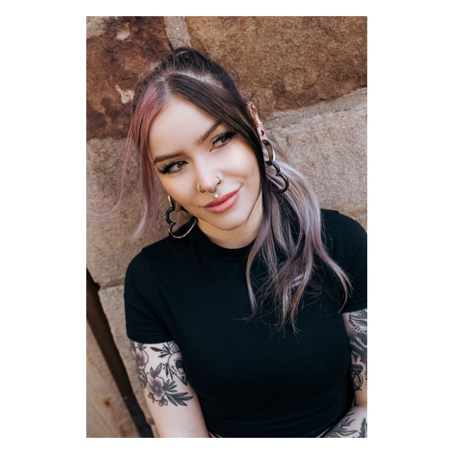 Oriental Sun Push-Fit Labret im Ohr Frau mit schwarzen und silbernen Ohrringen und Piercings, lächelnd vor einer Steinwand