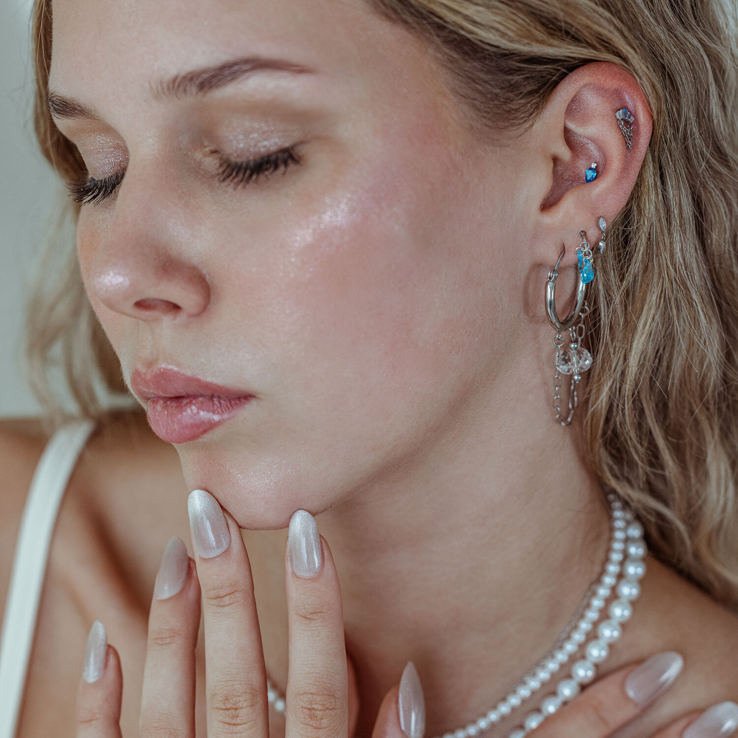 Mystic Dew Aufsatz Silber und Gold für Ohr Frau mit mehreren Ohrpiercings, darunter der Mystic Dew Aufsatz in Silber und Gold mit Lavendel- und Türkisfarbenen Kristallen, auf neutralem Hintergrund