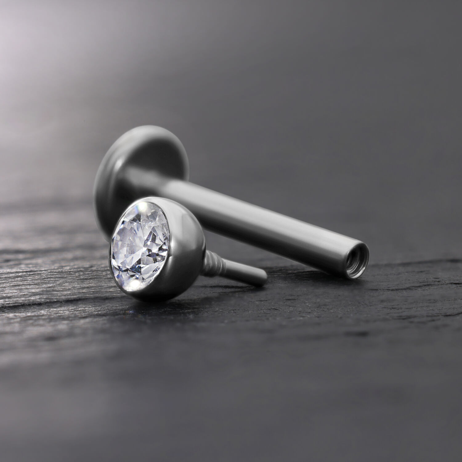 Silberner Labret-Aufsatz mit klarer Kristallkugel auf grauem Hintergrund