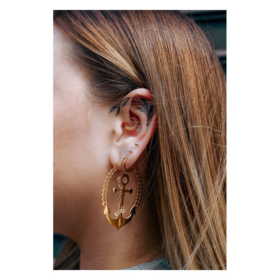 Goldene Ohrpiercings mit Anker und Kette, getragen am Ohr einer Frau.