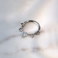 Septum Clicker mit Kristallherzen aus Titan Silberner Septum Clicker aus Titan mit Herzdesign und Kristallen auf marmoriertem Hintergrund