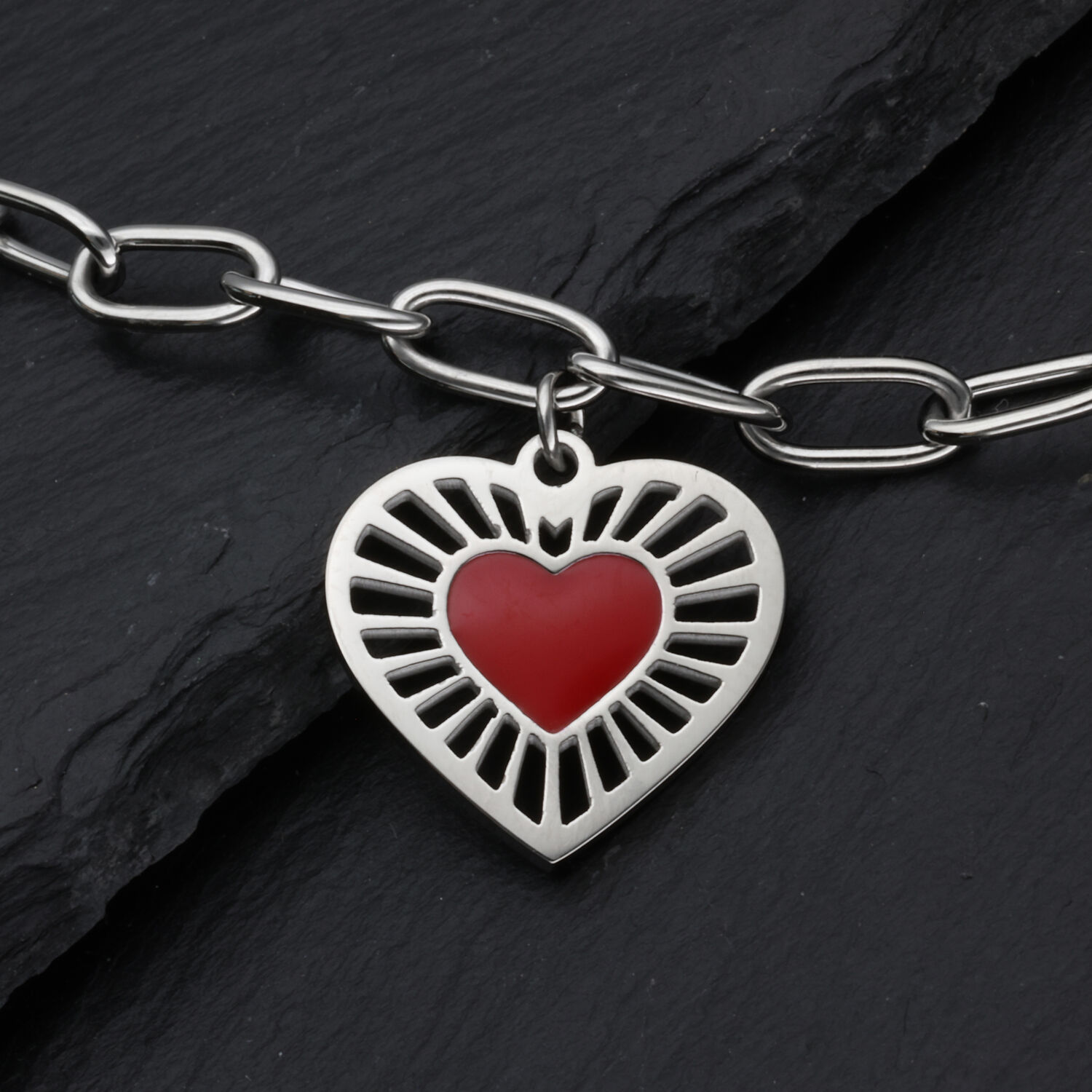 Silberfarbenes Sacred Heart Armband aus Edelstahl Silberfarbenes Armband mit rotem Herzanhänger auf dunklem Hintergrund