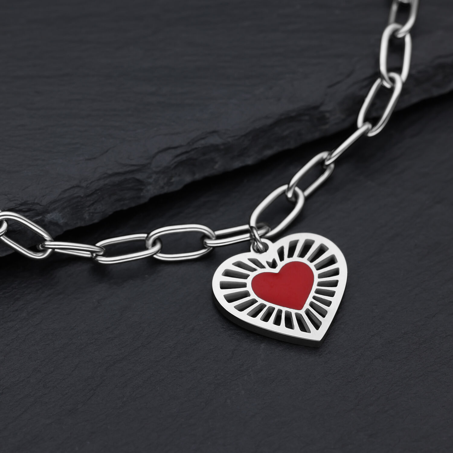 Silberfarbenes Sacred Heart Armband mit Herzanhänger Silberfarbenes Armband aus Chirurgenstahl mit rotem Herzanhänger auf dunklem Hintergrund
