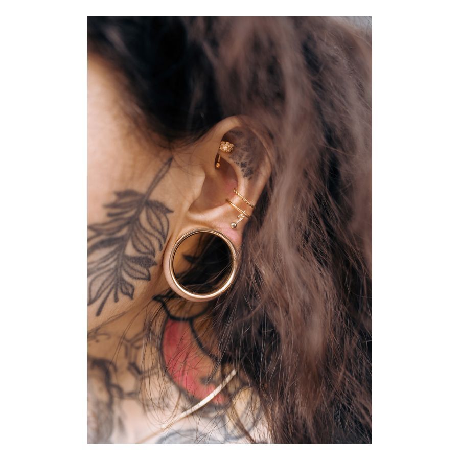 Stylisches Micro Bananabell Piercing in Roségold Roségoldenes Bananabell Piercing im Ohr mit Tattoo im Hintergrund