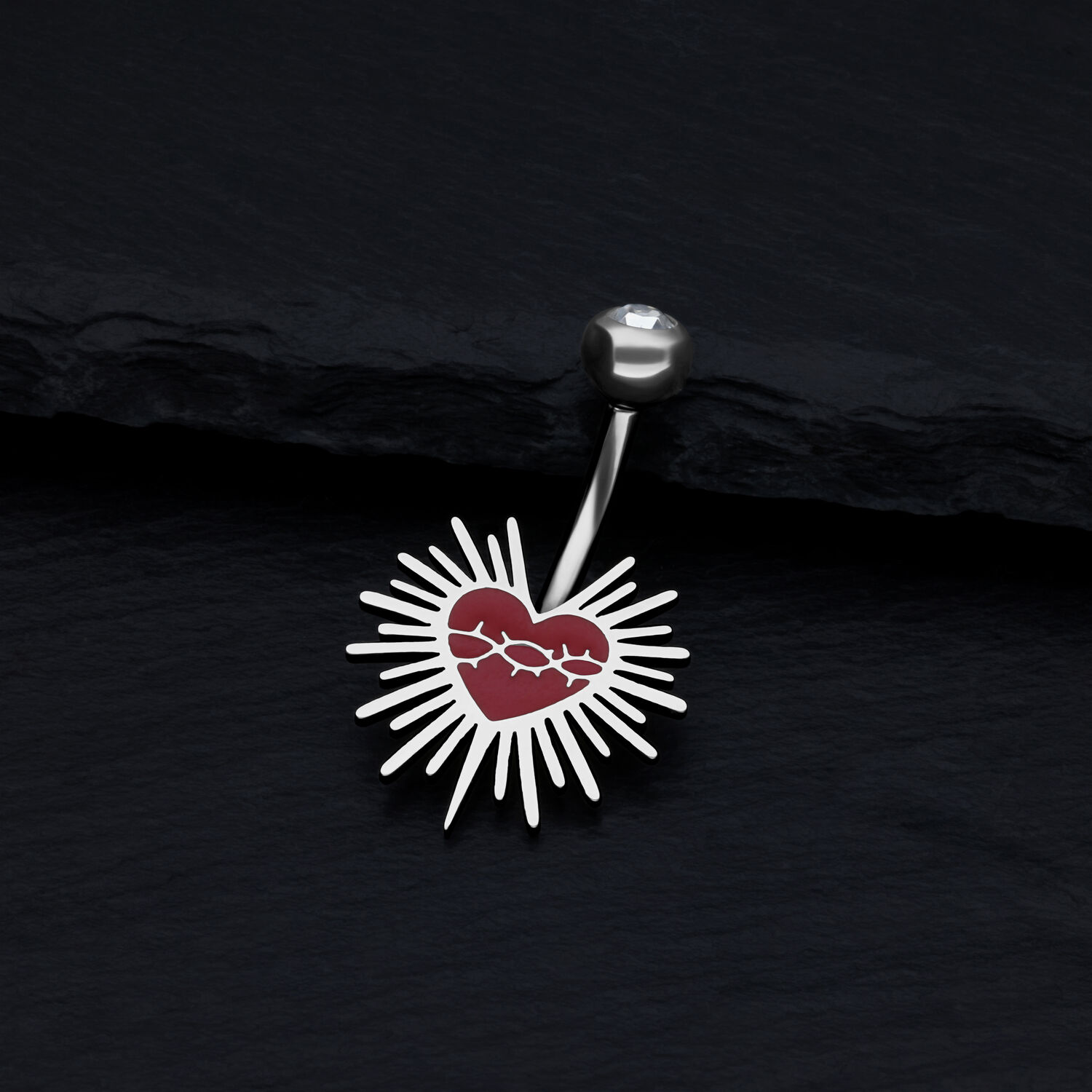 Bauchnabel Bananabell mit Herz-Design aus Titan Silbernes Bauchnabel Bananabell mit rotem Herz und Strahlen auf schwarzem Hintergrund