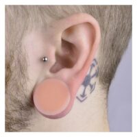 Kaos Softwear Hider Plug in Ohr getragen Hautfarbener Silikon Plug im Ohr getragen, Tattoo sichtbar, heller Hintergrund