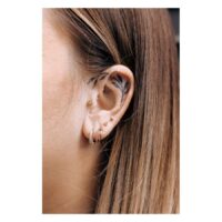 Triangle Barbell in Gold am Ohr Goldenes Triangle Barbell Piercing am Ohr einer Person mit weiteren Piercings und Ohrtattoo