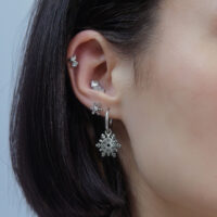 Silberner Schneeflocken-Aufsatz für Piercings Ohr mit mehreren silbernen Piercings, Schneeflocken-Design, auf neutralem Hintergrund