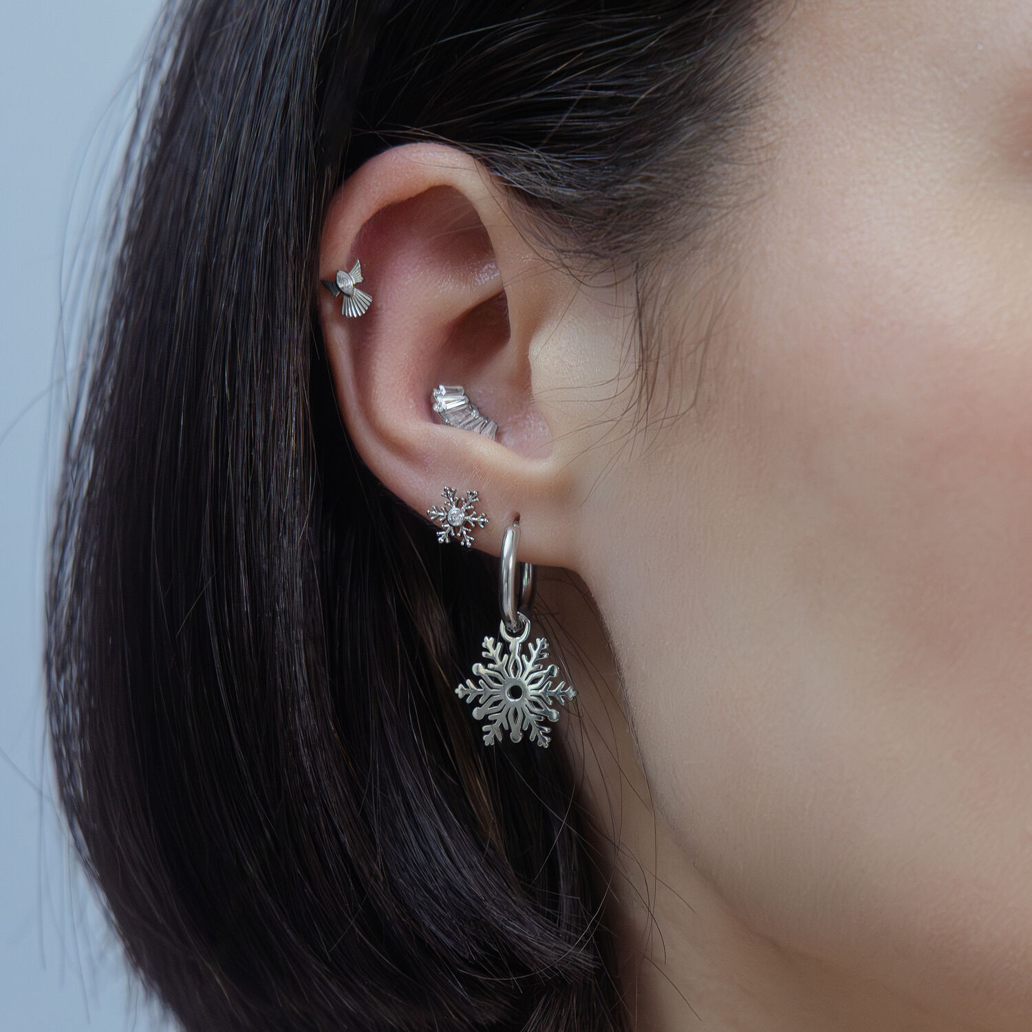 Silberner Schneeflocken-Aufsatz für Piercings Ohr mit mehreren silbernen Piercings, Schneeflocken-Design, auf neutralem Hintergrund