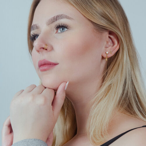 Frau mit goldenem Clicker-Piercing im Ohr, seitliches Profil auf hellem Hintergrund
